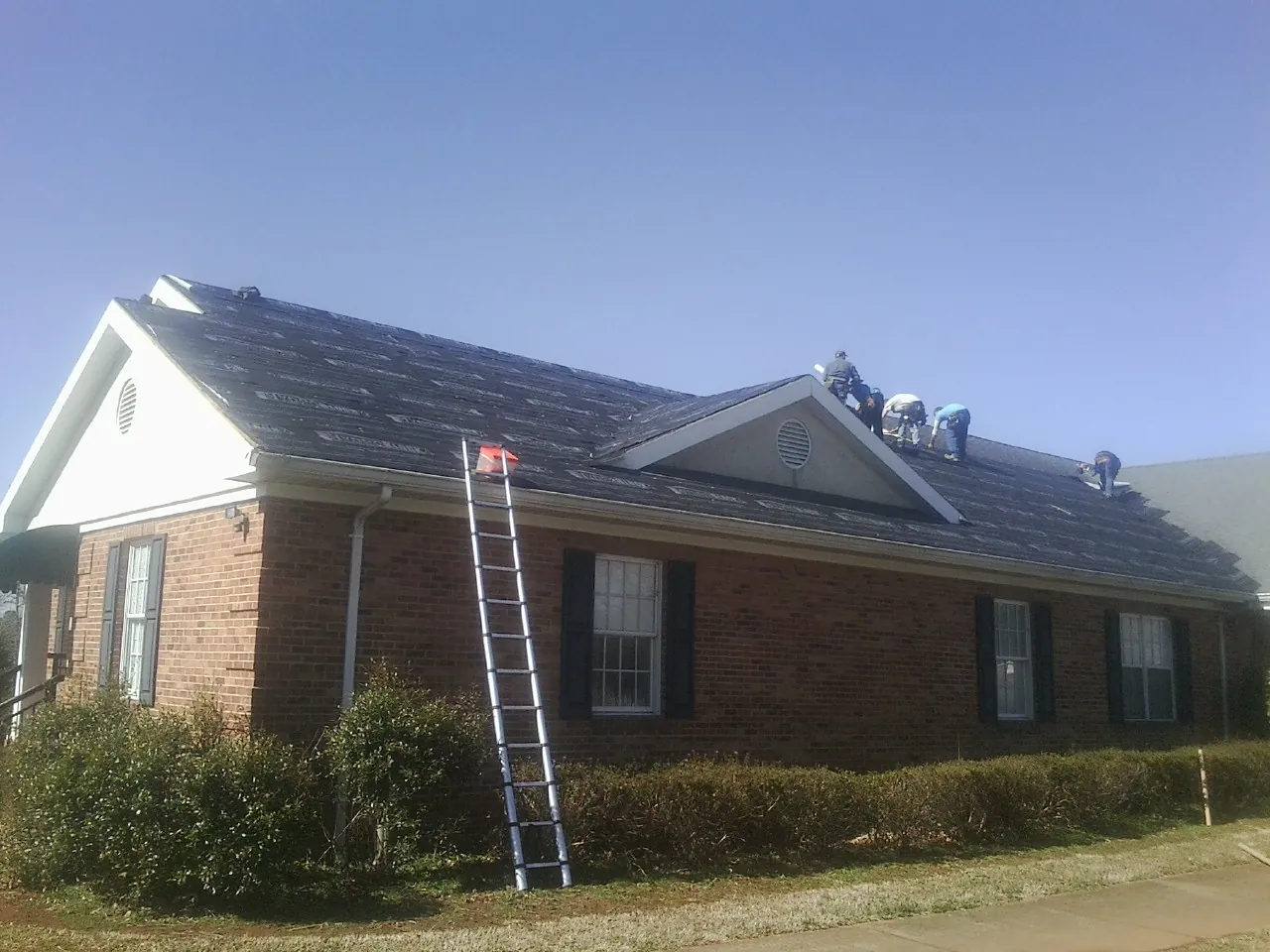 Crew tearing shingles off a brick ranch roof with a ladder set — Emergency Roof Repair work by our crew in Albertville