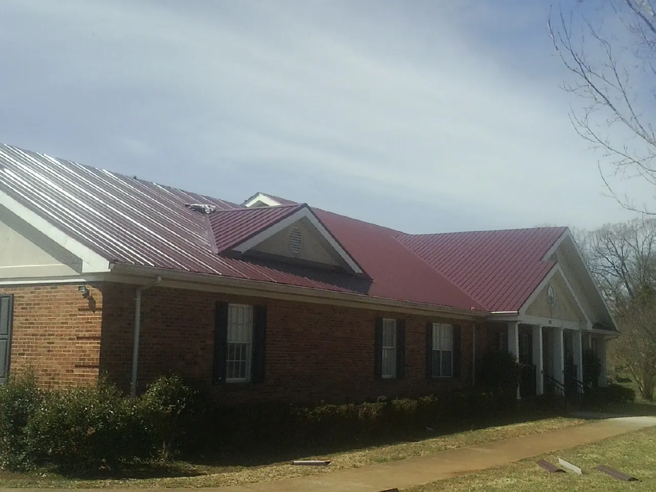 Red metal roof with gabled entries on a long brick building, from a Hail Damage Roof Repair job in Albertville