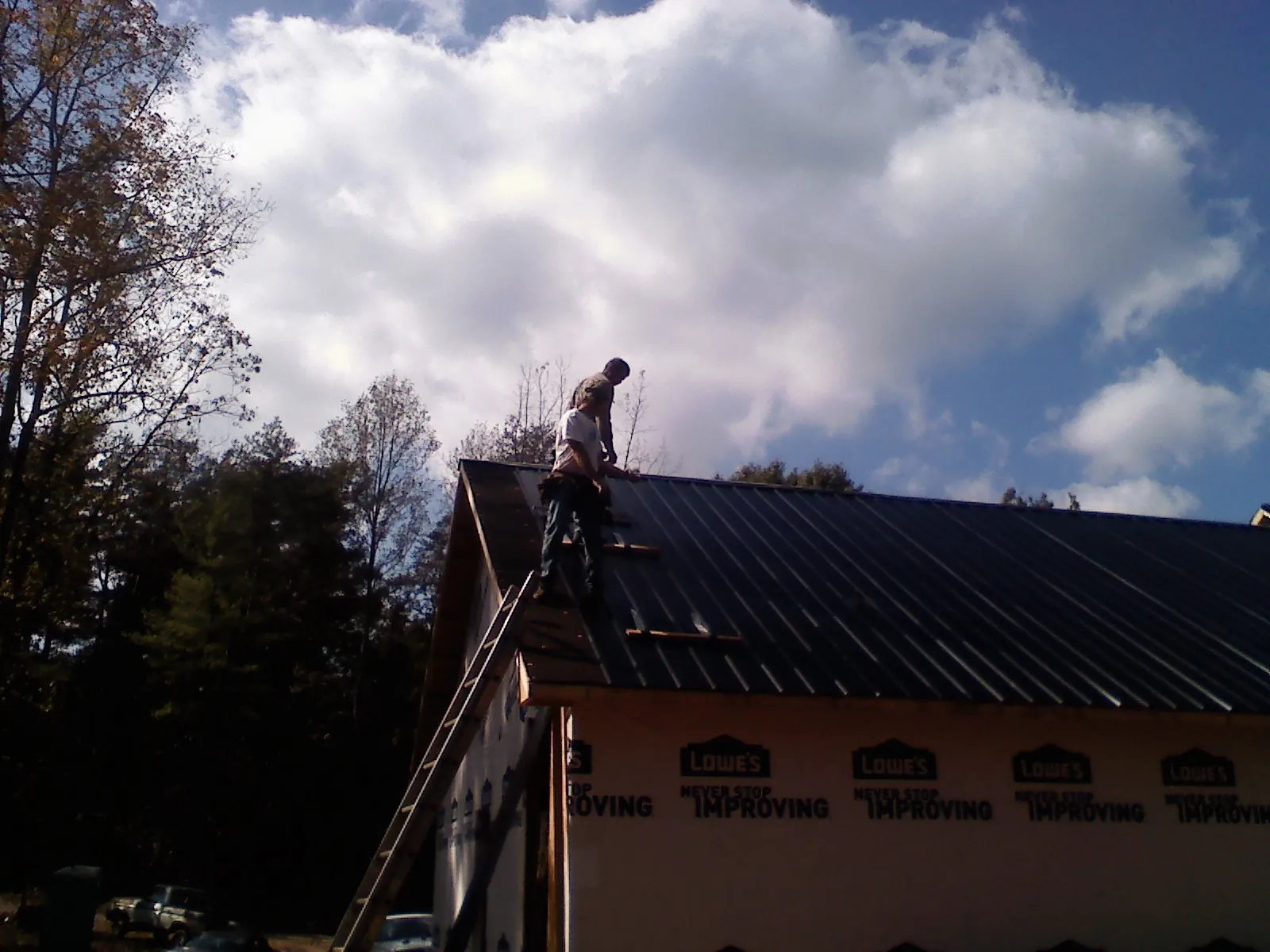Roofer fastening dark metal panels high against a cloudy sky, from a Roof Inspection job in Albertville